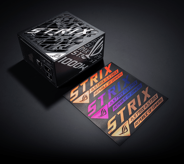 Чорний блок живлення ROG Strix 1000W, зображений під кутом на темному тлі, поруч із ним розміщено три кольорові наклейки з логотипом Strix.